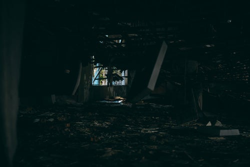 暗がりから見る天井が崩れ落ちる廃墟の写真