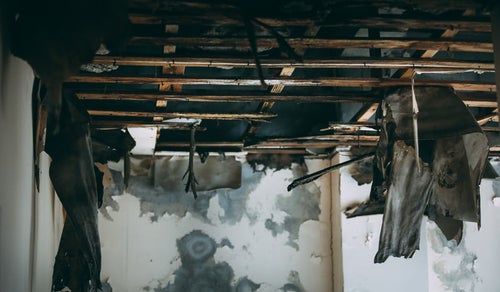 崩れ落ちた天井から下がるすすけたカーテンの写真