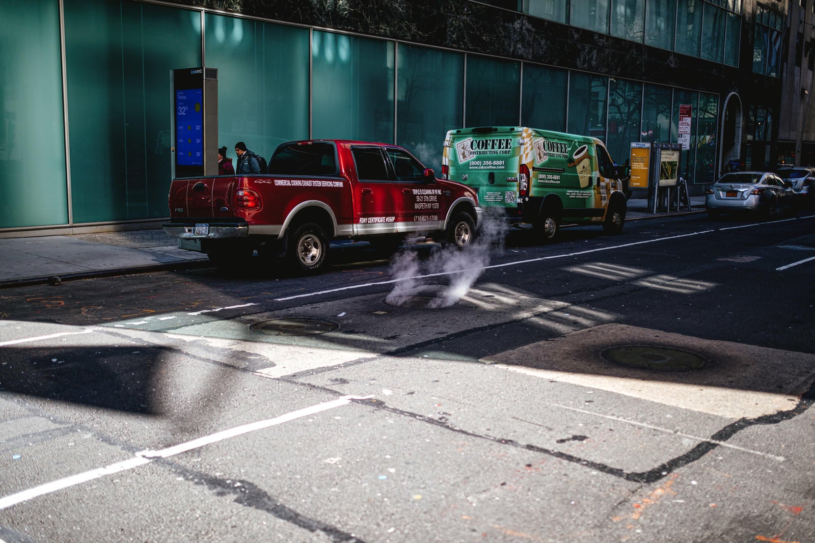 「マンホールから立ち上る煙と路上駐車」の写真