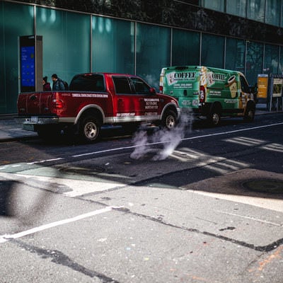マンホールから立ち上る煙と路上駐車の写真
