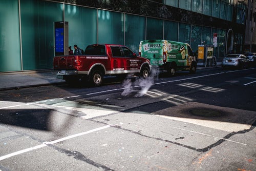 マンホールから立ち上る煙と路上駐車の写真