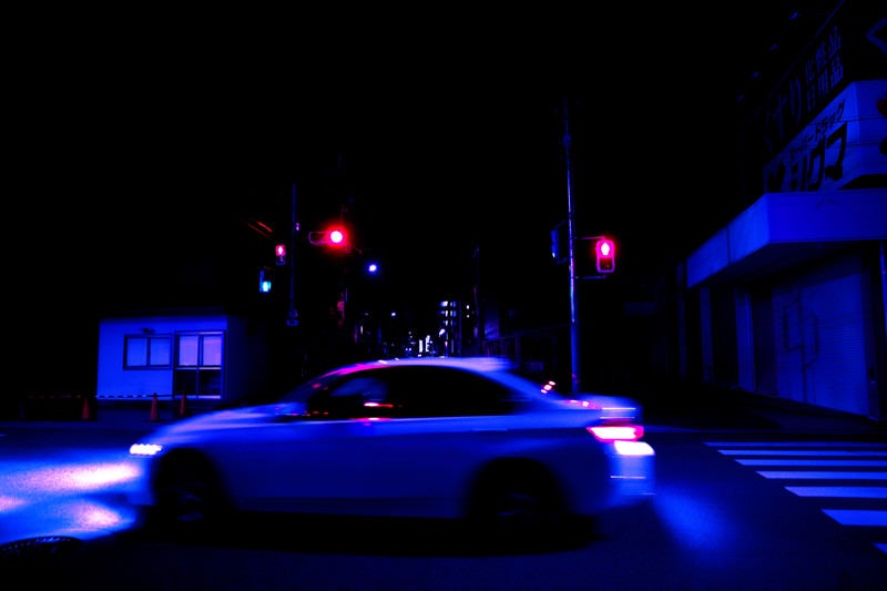 深夜の交差点を走り去る自動車の写真