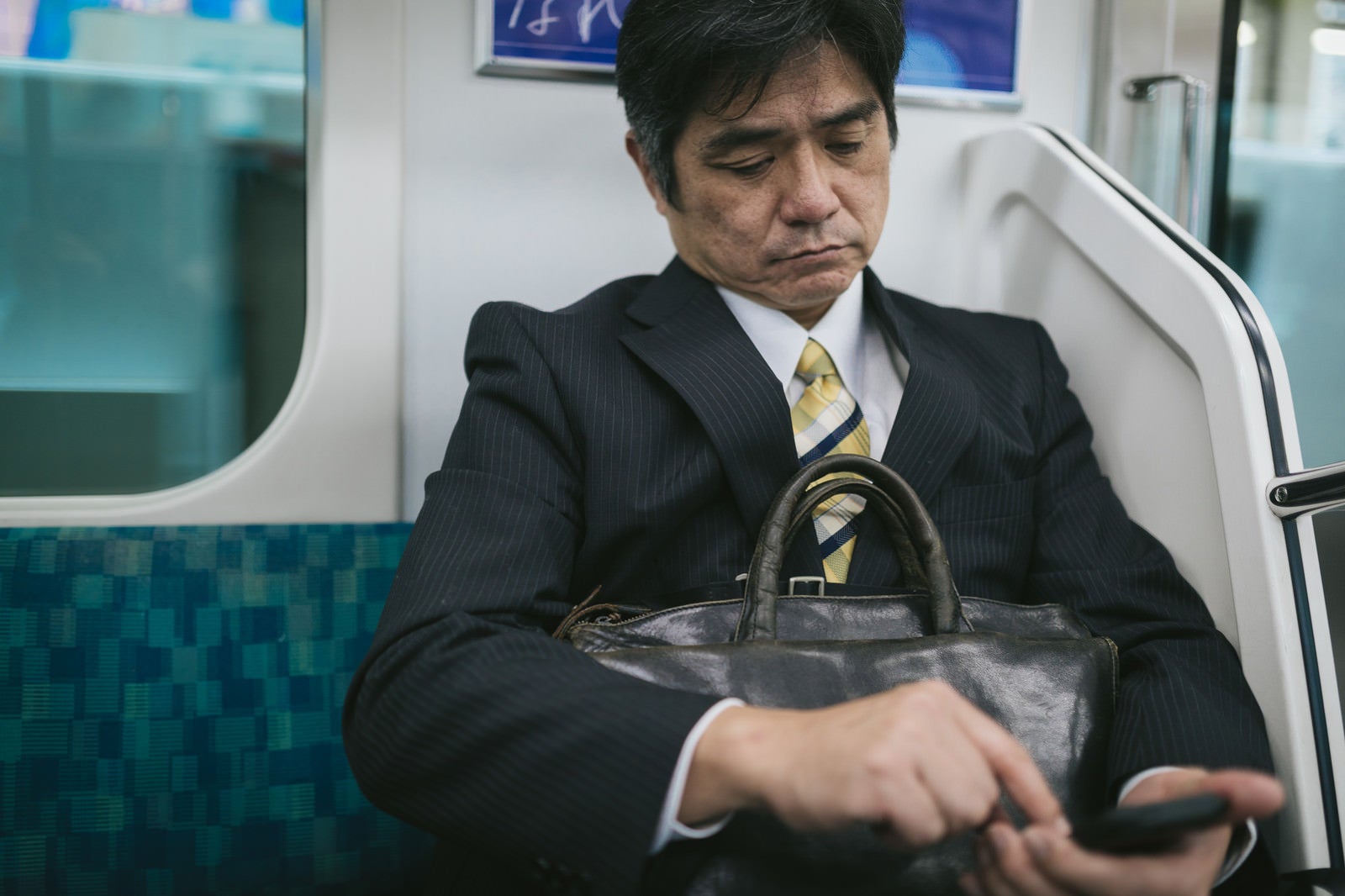 「通勤中にニュースアプリを確認するサラリーマン」の写真［モデル：よたか］