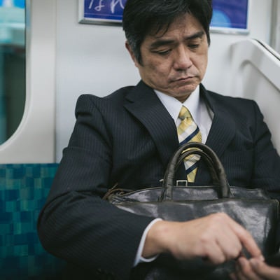 通勤中にニュースアプリを確認するサラリーマンの写真