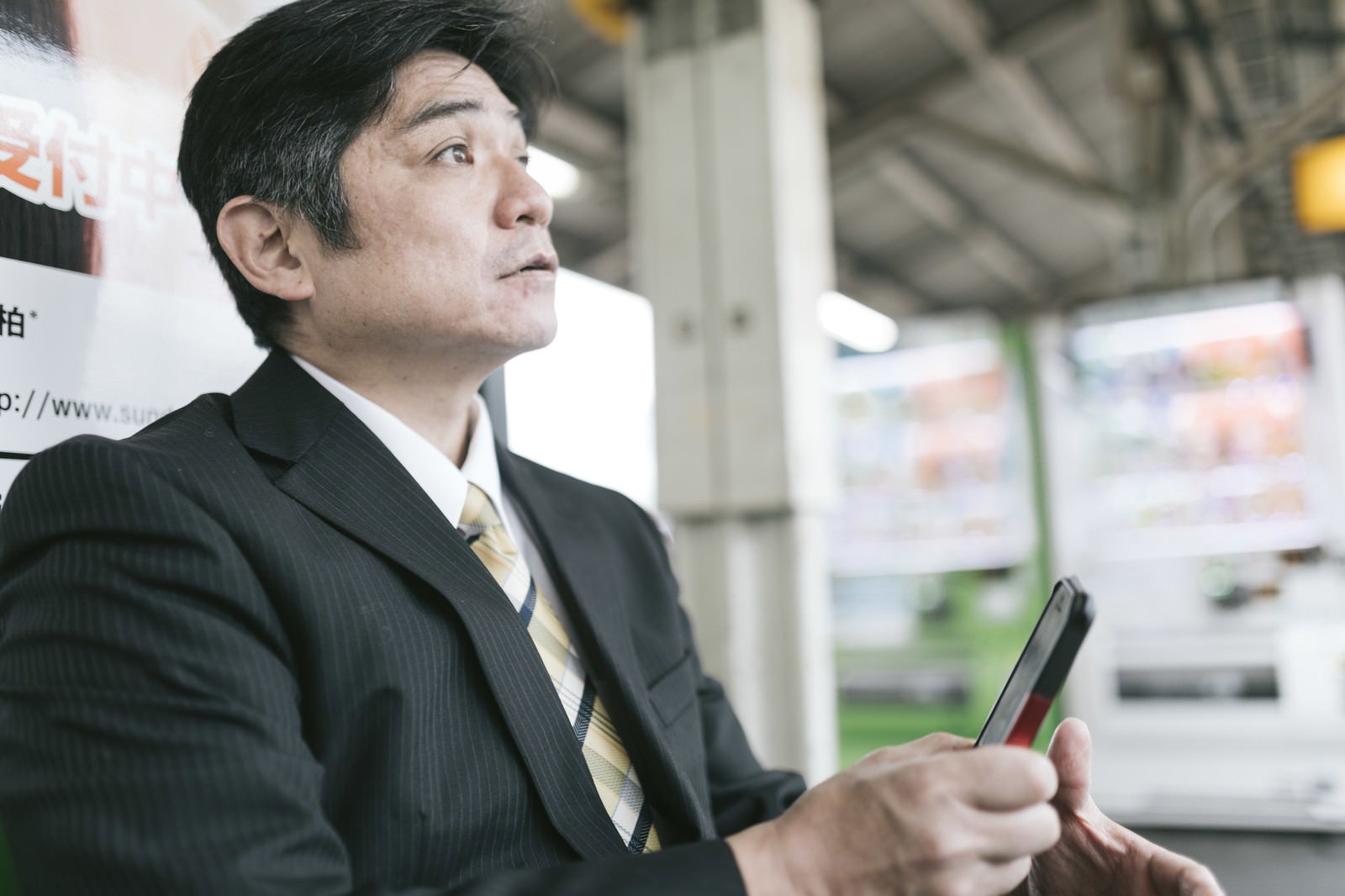 「駅のベンチでスマホに熱中してて電車がいってしまった上司」の写真［モデル：よたか］