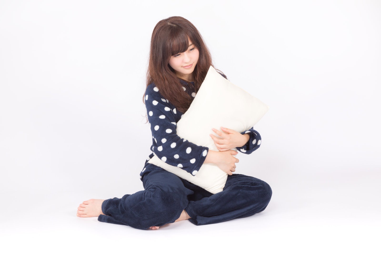 「枕を抱いて眠そうな表情の若いパジャマ姿の女性」の写真