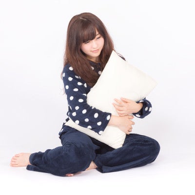 枕を抱いて眠そうな表情の若いパジャマ姿の女性の写真