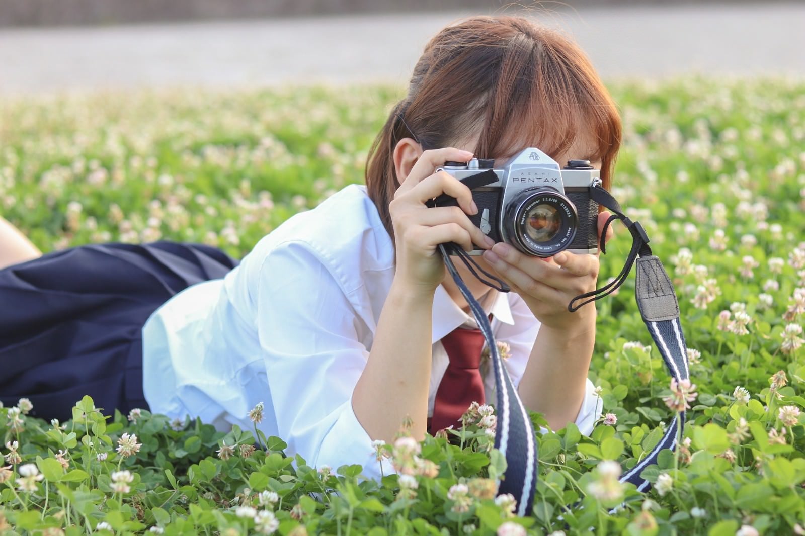「草原にうつ伏せてカメラを構える女子高生」の写真