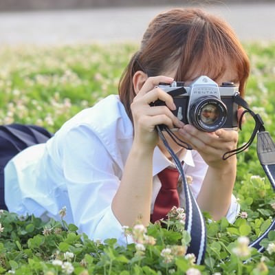草原にうつ伏せてカメラを構える女子高生の写真