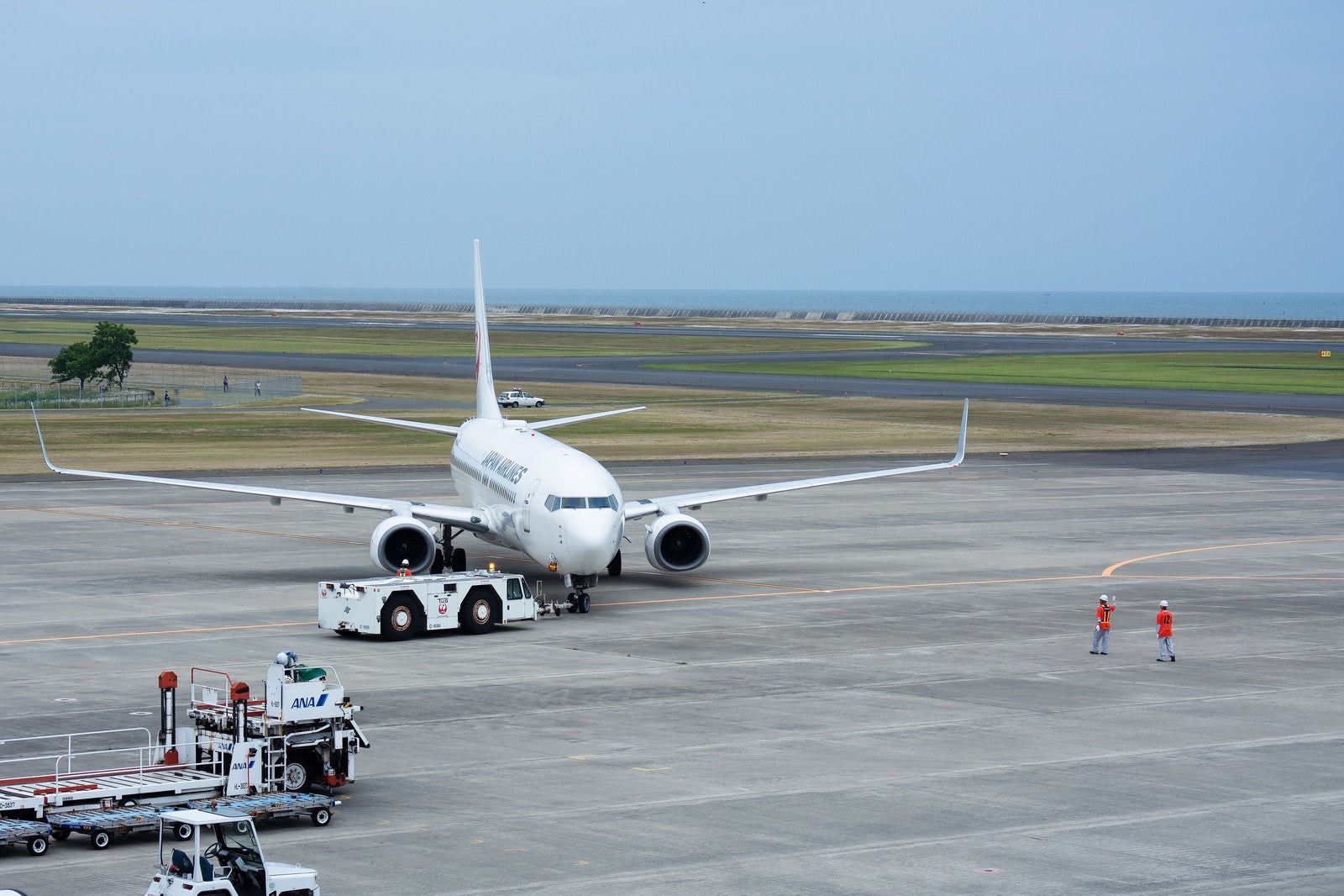 「駐機場を離れプッシュバックされる飛行機と誘導するグランドハンドラー（山口宇部空港）」の写真
