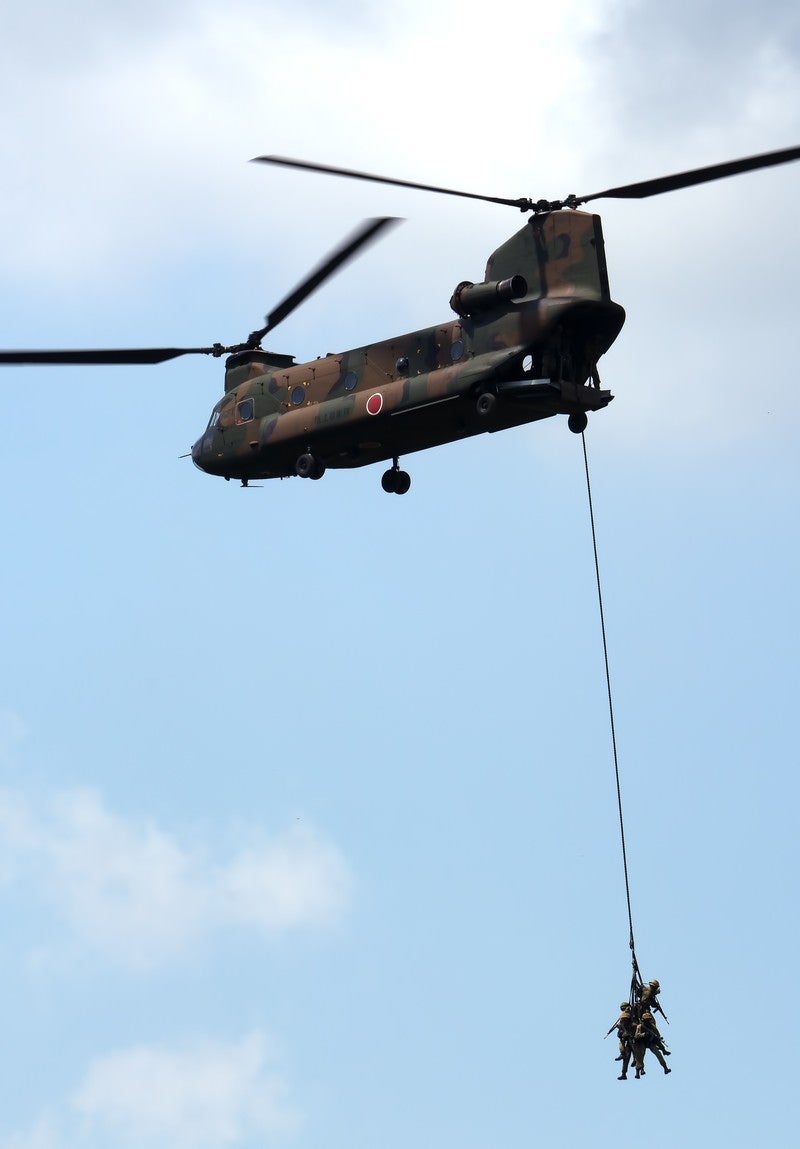 「周囲を警戒しながら、CH-47に吊り下げられ撤収する隊員。」の写真