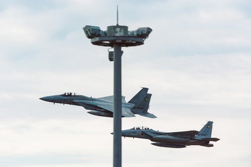 鉄塔被りの併走する戦闘機（F-15）の写真
