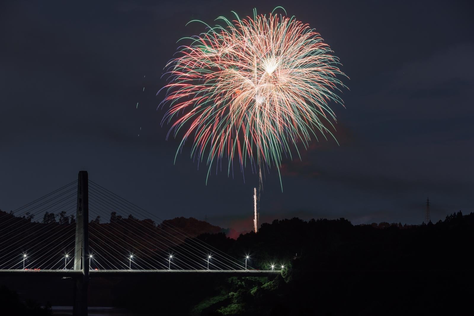 「夜空を彩る打ち上げ花火と春田大橋」の写真