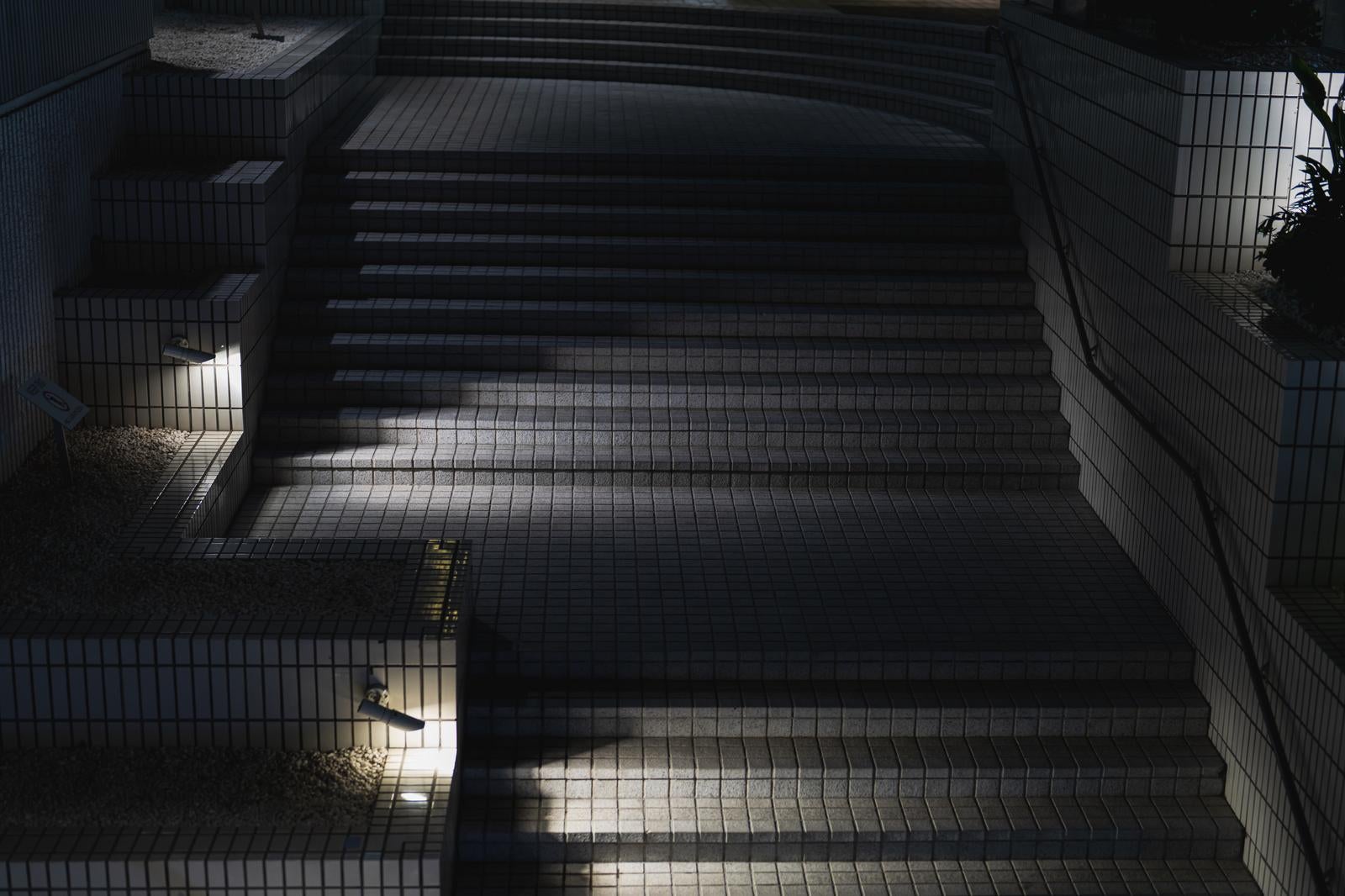 日光が差し込むタイル張りの階段、両側にフェンスと手すりがある公共施設の通路