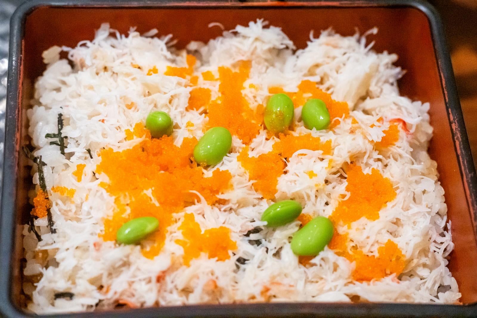 蟹のほぐし身ととびこ、枝豆を散らした重箱入りのちらし寿司のアップ写真