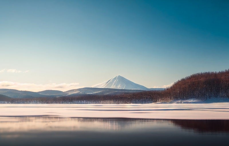 静寂な冬の湖畔と雪山の写真