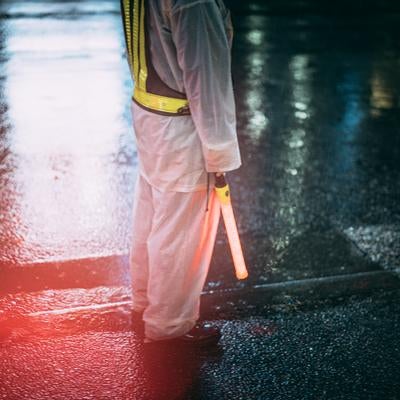 夜の雨に濡れた歩道に立つ交通誘導員の写真