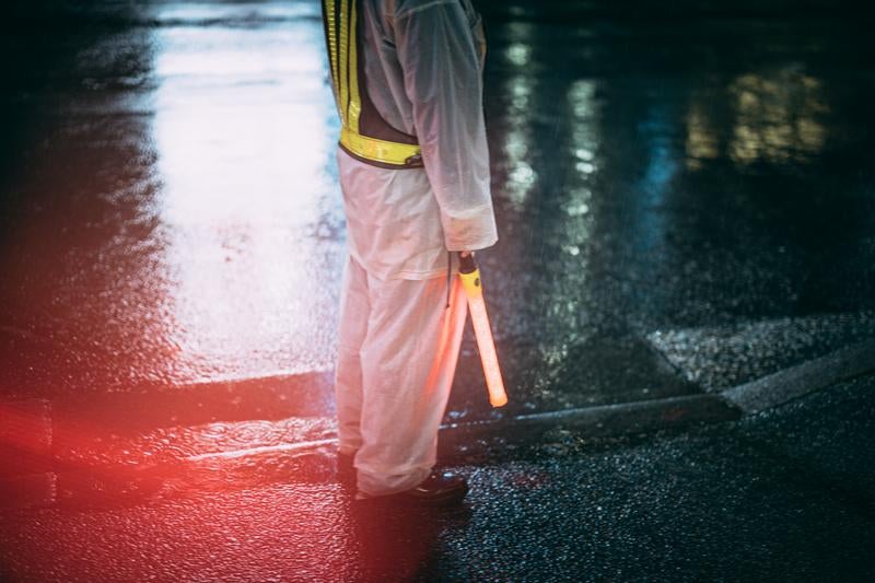 夜の雨に濡れた歩道に立つ交通誘導員の写真