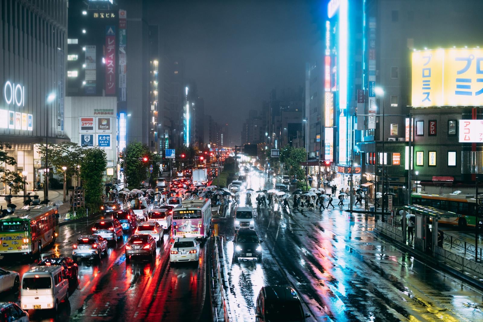 「雨で濡れた夜の交差点の賑わいと信号待ちする車のテールランプ」の写真