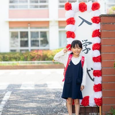 入学式で校門の前、ピースする小学生の女の子の写真