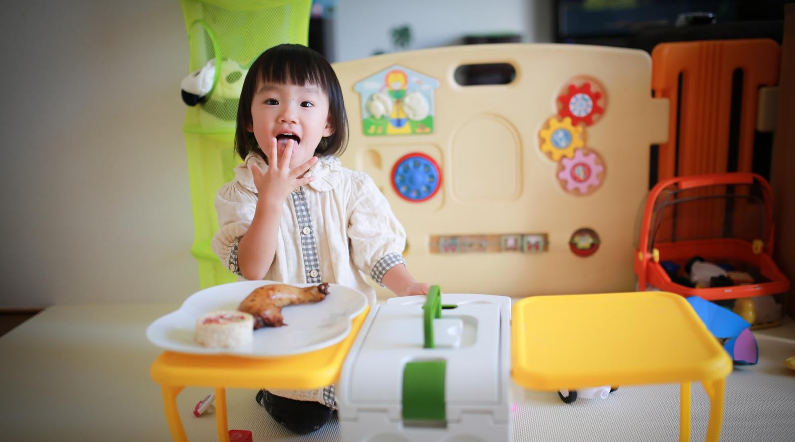 ベージュのテーブルでおやつを食べながら舌を出して笑う女の子