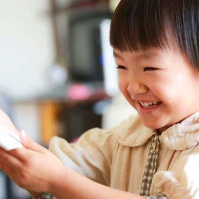 ベージュの羽織をしたショートヘアの女の子が笑顔でタブレットを見るの写真