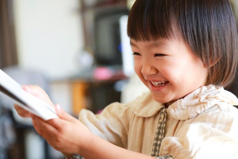 ベージュの羽織をしたショートヘアの女の子が笑顔でタブレットを見る