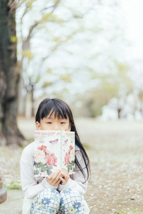 公園で洋書を広げる女の子の写真