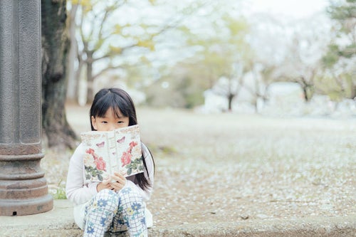 公園で洋書を読む女の子の写真