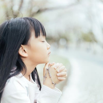 ロザリアを握り祈るクリスチャンの子供の写真