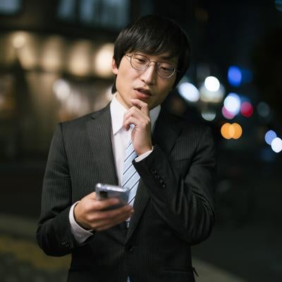 屋外でスマートフォンをチェックする男性の写真