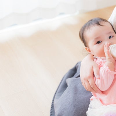 ママに抱かれて哺乳瓶でミルクを飲む赤ちゃんの写真