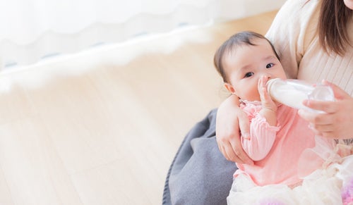 ママに抱かれて哺乳瓶でミルクを飲む赤ちゃんの写真