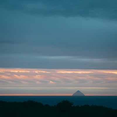 淡い朝焼けの中にシルエットが浮かぶ南硫黄島の写真