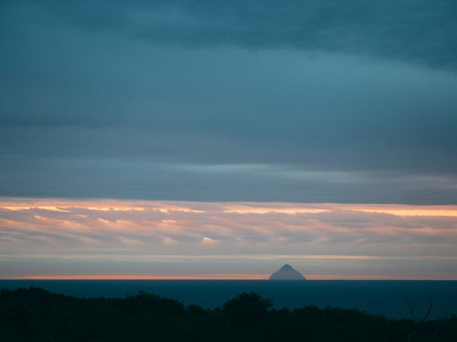 淡い朝焼けの中にシルエットが浮かぶ南硫黄島の写真