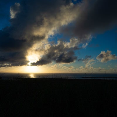 夕陽に照らされる遠くに見える海岸の釜岩と細長い姿が海にうかぶ監獄岩の写真
