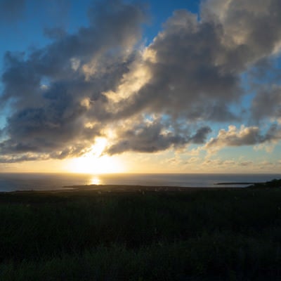 南の海に沈む太陽と釜岩に向かって海面に伸びる太陽の道の写真