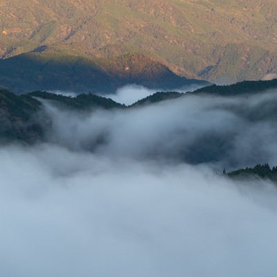 朝日に照らされ輝く山々と雲海に静かに沈む山々の写真