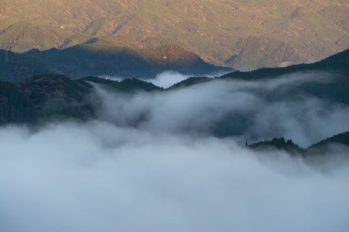 朝日に照らされ輝く山々と雲海に静かに沈む山々の写真