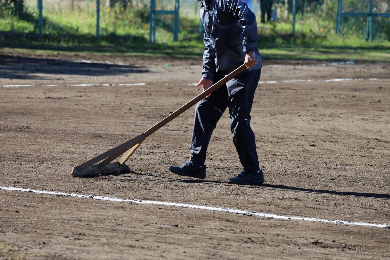 野球場でトンボを使ってグラウンドの土を平らに整備する作業員の男性