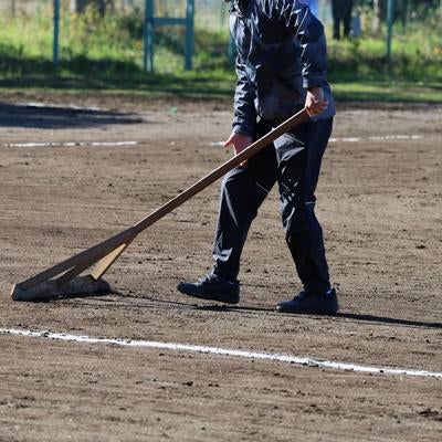 レーキを使って野球場のグラウンドを整備する作業員の写真