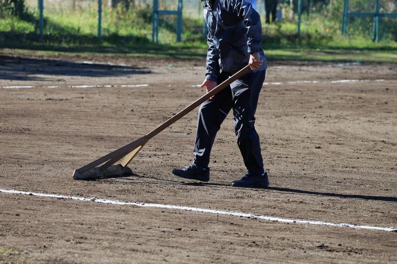 レーキを使って野球場のグラウンドを整備する作業員の写真