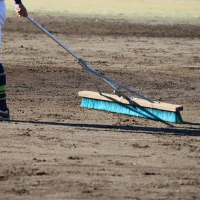 青いブラシでグラウンドの土を整備する野球場スタッフの写真