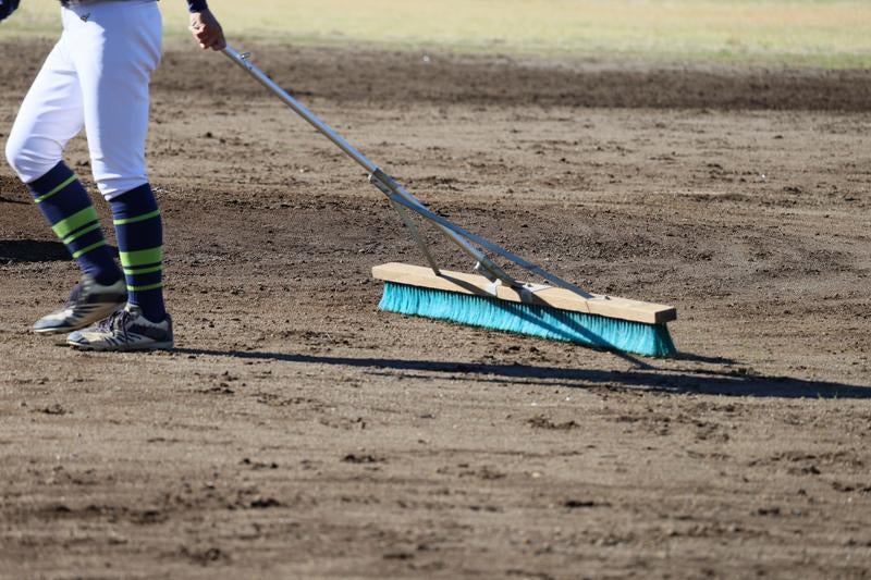 青いブラシでグラウンドの土を整備する野球場スタッフの写真