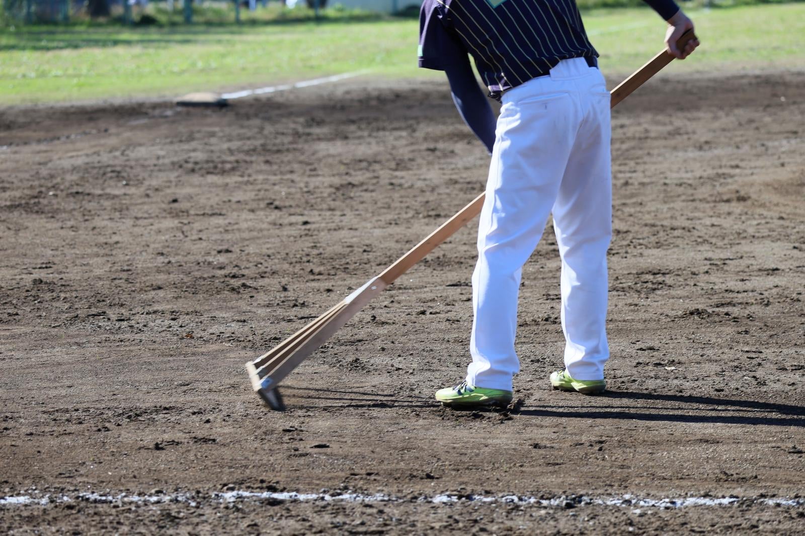 野球場でレーキを使ってグラウンドの土を整備する作業員