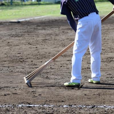 野球場でレーキを使ってグラウンドを整備する作業員の様子の写真