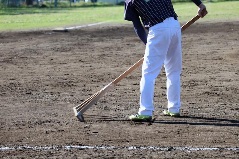 野球場でレーキを使ってグラウンドを整備する作業員の様子の写真