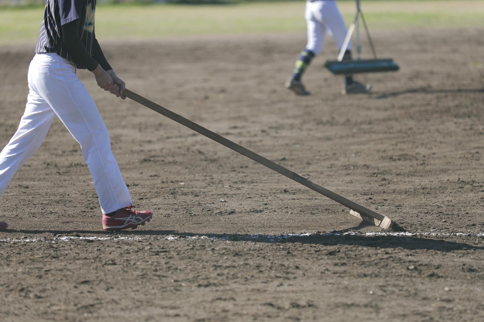 野球場でトンボを使ってグラウンド整備をする白い作業服の人
