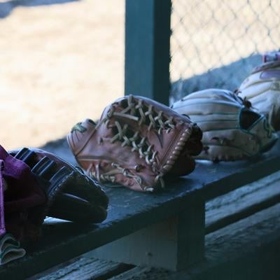 木製ベンチに並ぶキャッチャーミットとバッティングヘルメットの写真