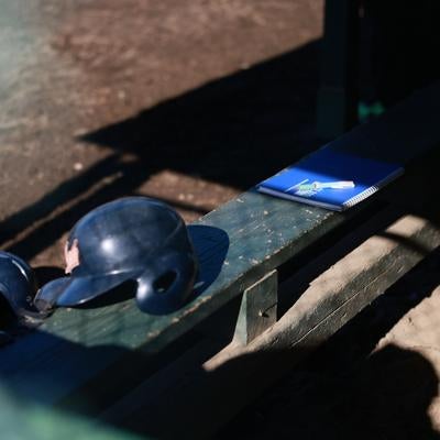 木製ベンチに置かれた黒いヘルメットと茶色いキャッチャーミットの写真